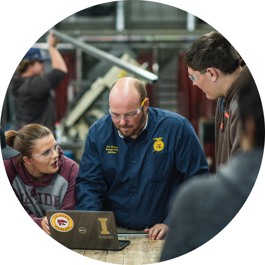 An instructor and students wearing safety goggles in a workshop.