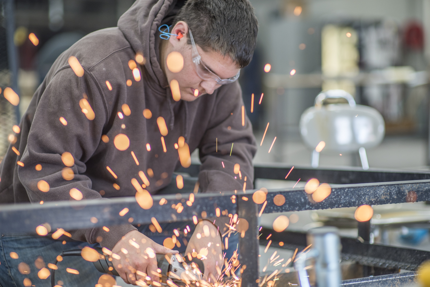 A man wearing goggles and ear plugs using a saw that is throwing sparks.