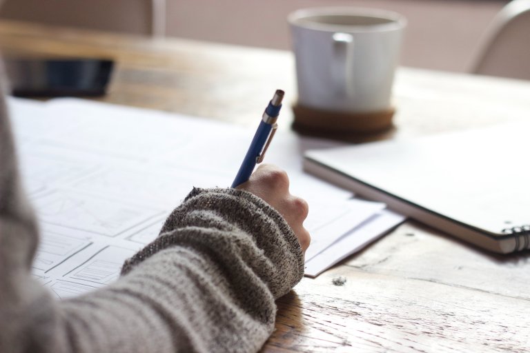 A desk with homework and a student's hand holding a pen